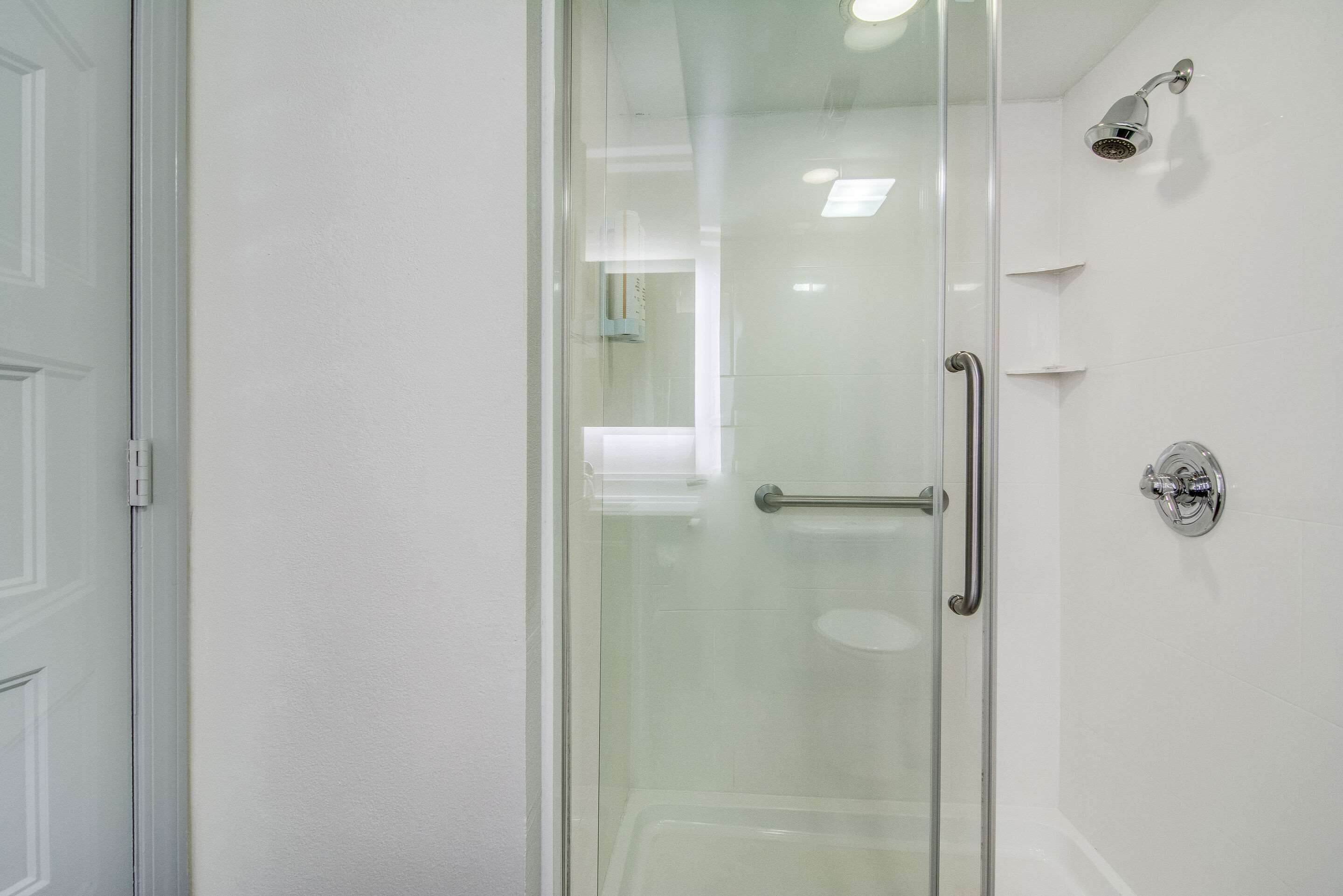 A modern bathroom with a glass-enclosed shower, a white tiled wall, and a chrome showerhead.