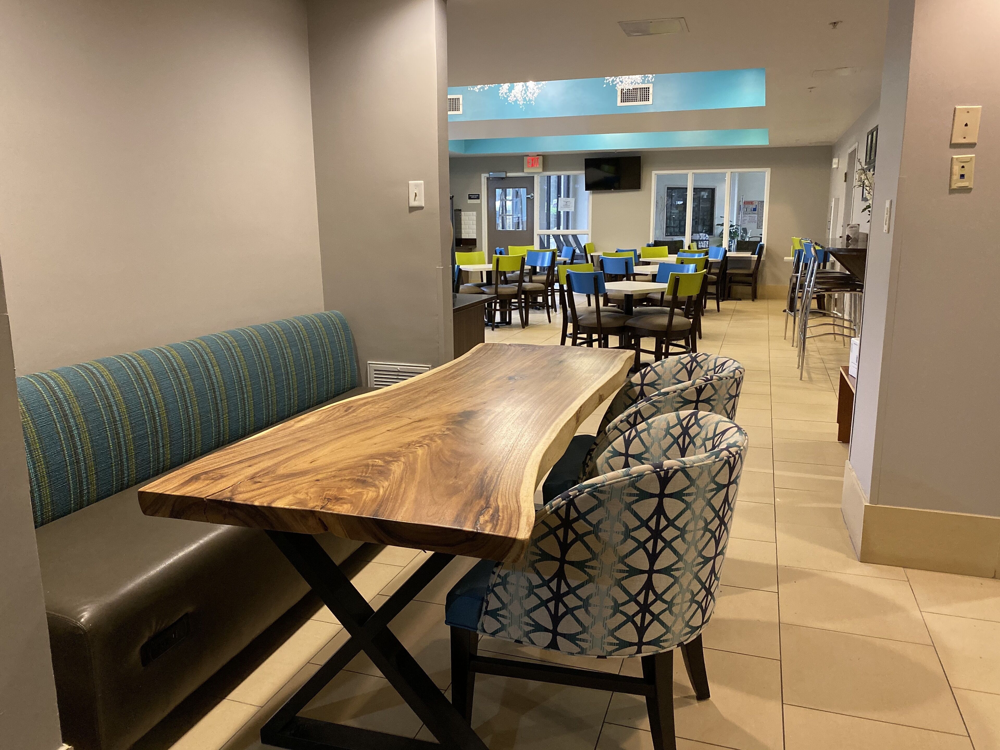 A dining area with a wooden table and bench, patterned chairs, and a blue wall with a window.