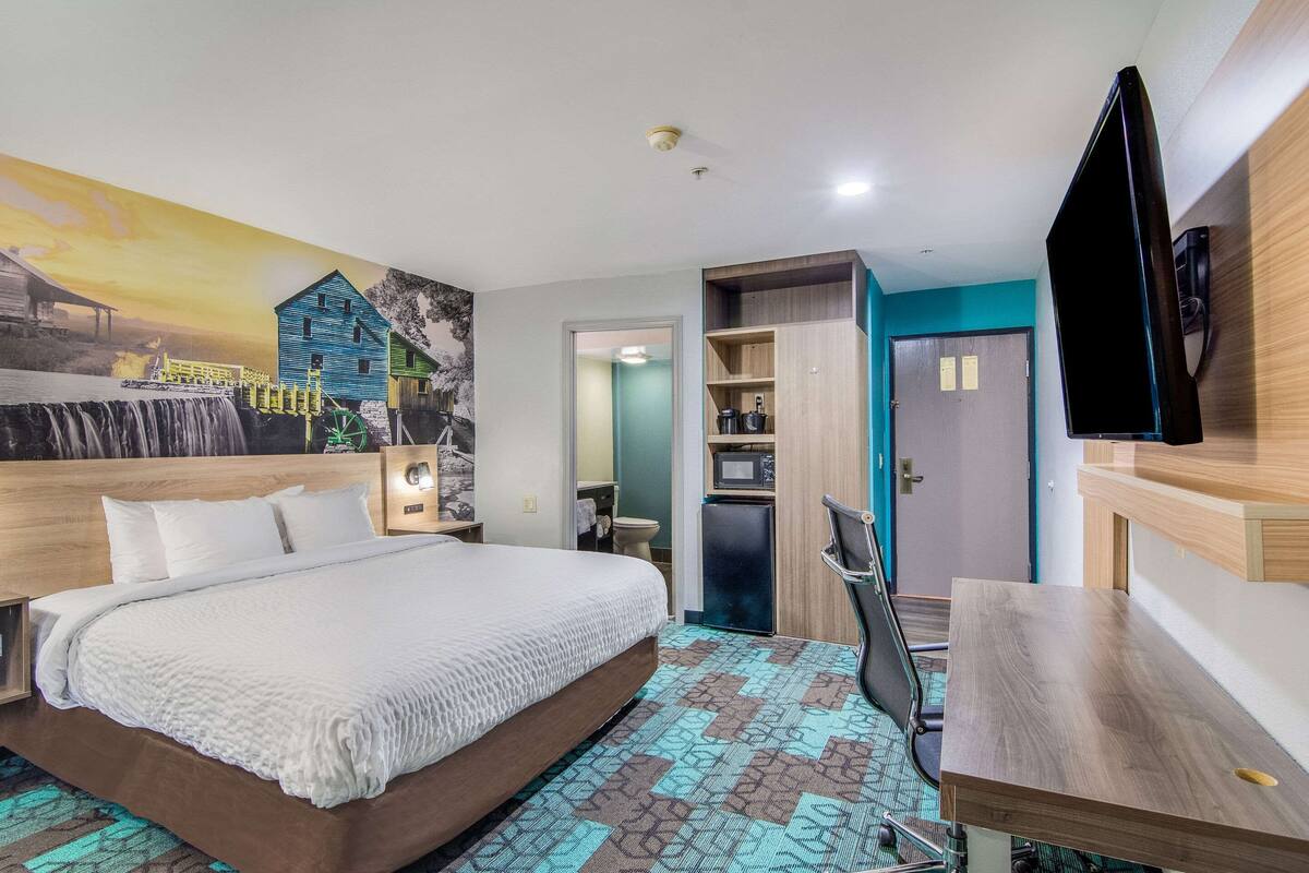 A hotel room with a large bed, a desk, a TV, a microwave, and a small refrigerator.