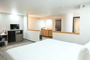 A hotel room with a bed, a desk with a television, a microwave, and a wardrobe.