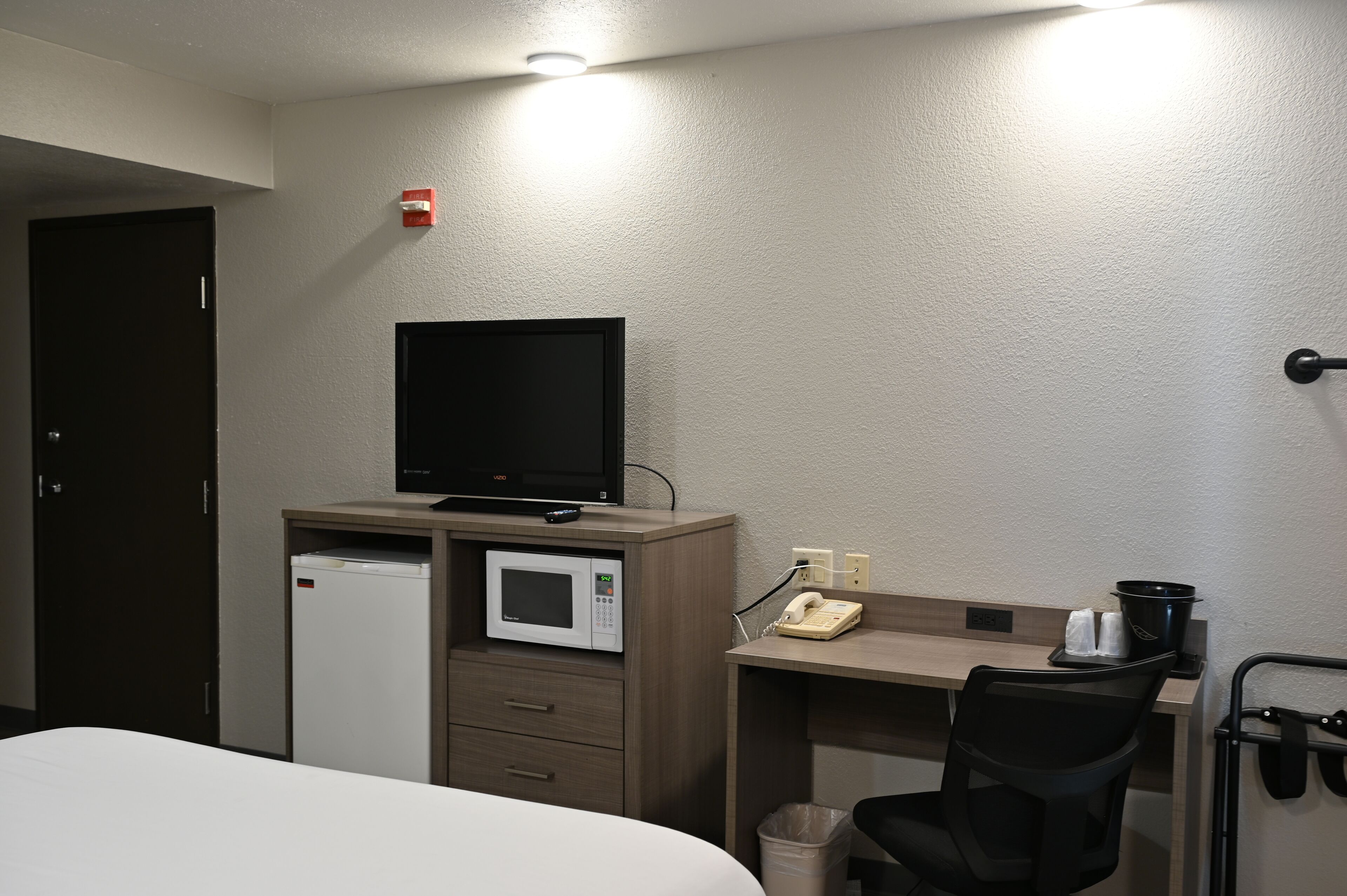 Habitació d'hotel amb un llit, un escriptori amb un monitor d'ordinador, un microones, un telèfon i un safataire.