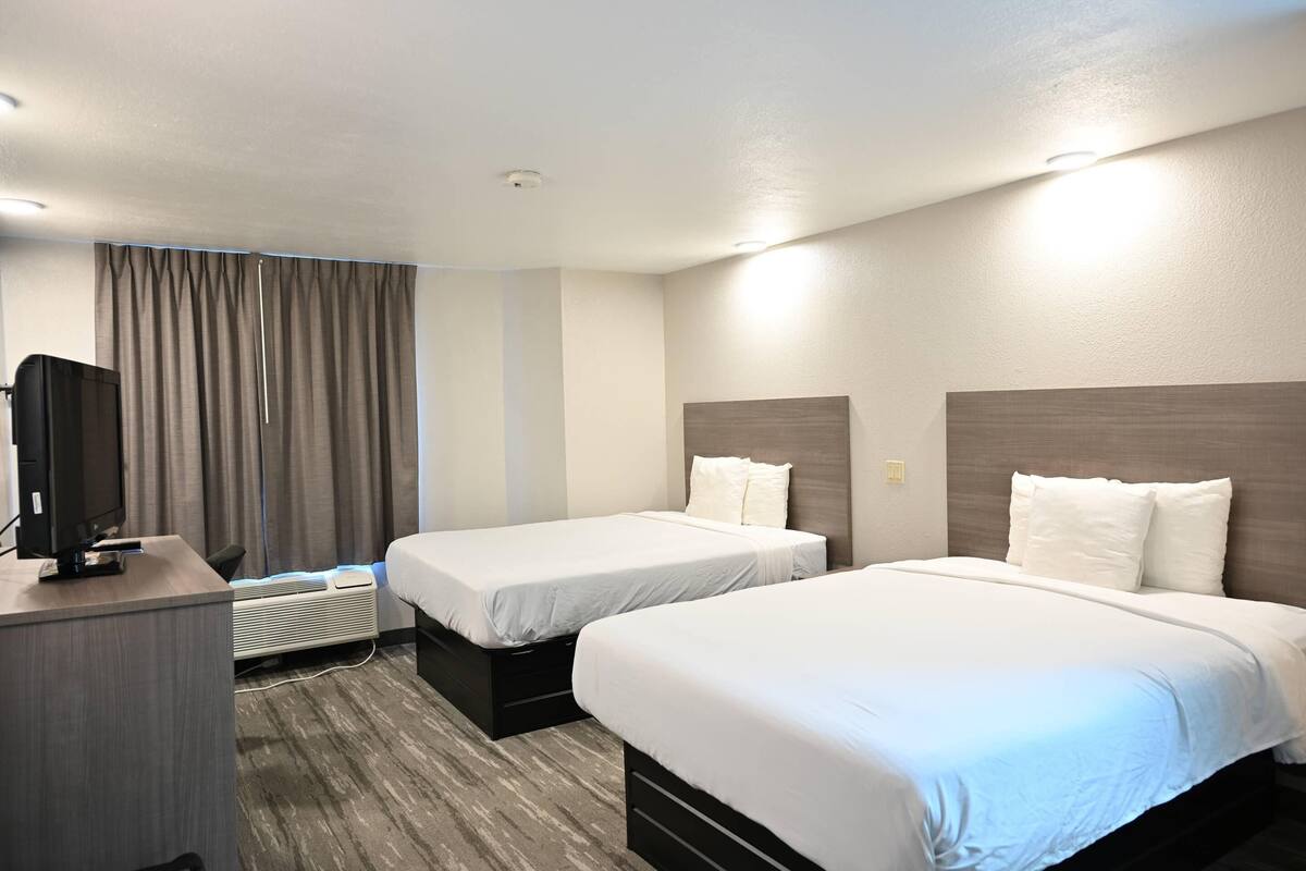 A hotel room with two beds, a desk, a television, and a window with curtains.