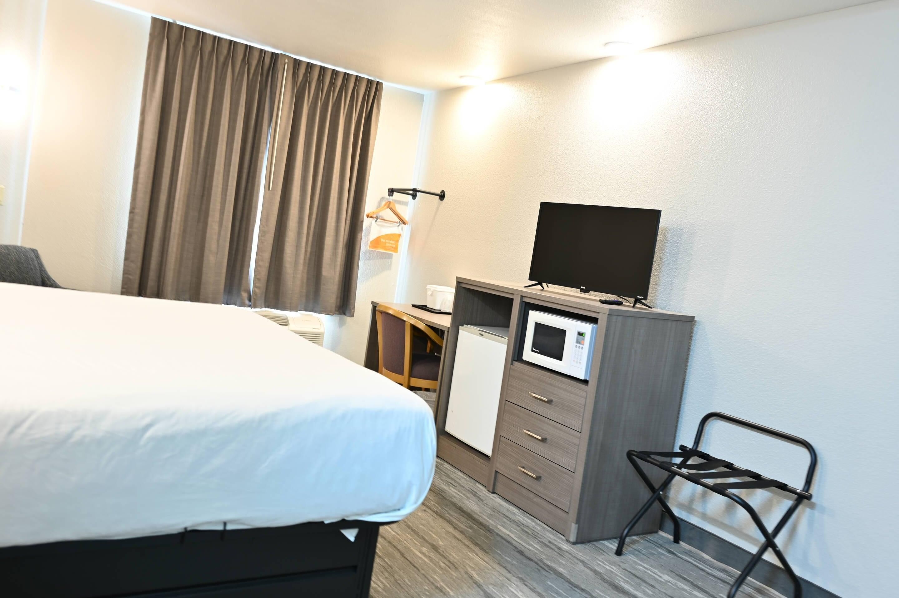 A hotel room with a bed, a desk with a microwave, a TV, and a chair.