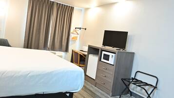 A hotel room with a bed, a desk with a microwave, a TV, and a chair.