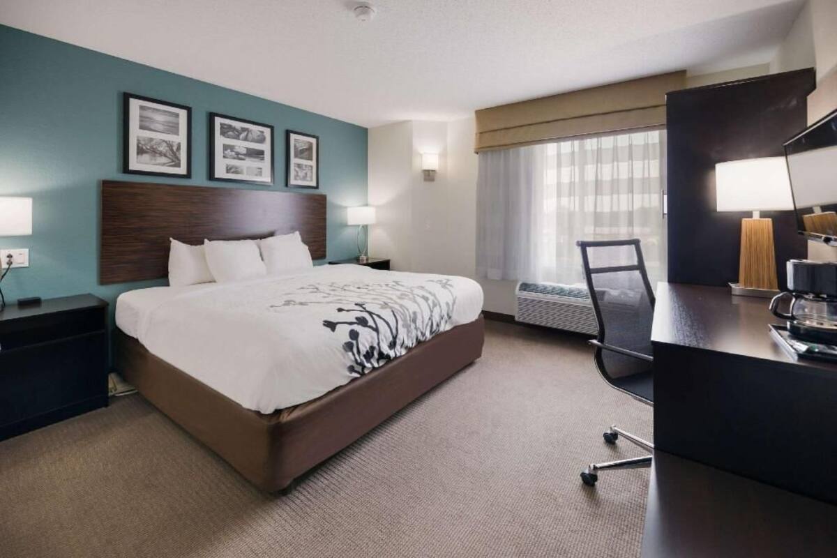 A hotel room with a large bed, a desk, a chair, a desk lamp, and a window with curtains.