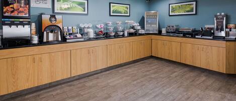 A coffee shop counter with a fruit juice dispenser, a coffee machine, and a display of coffee cups.