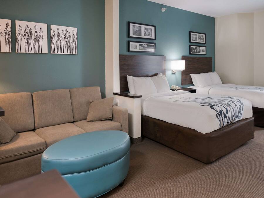 Een hotelkamer met een bank, twee bedden, een nachtkastje en wanddecoratie.
