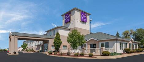 A Sleep Inn & Suites hotel with a central tower, a covered entrance, and well-maintained landscaping.