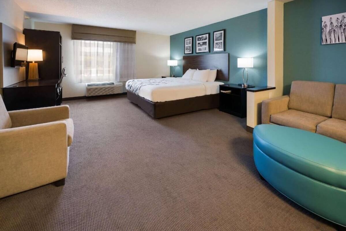 A hotel room with a bed, two bedside tables, a desk, a chair, a sofa, and a window with curtains.