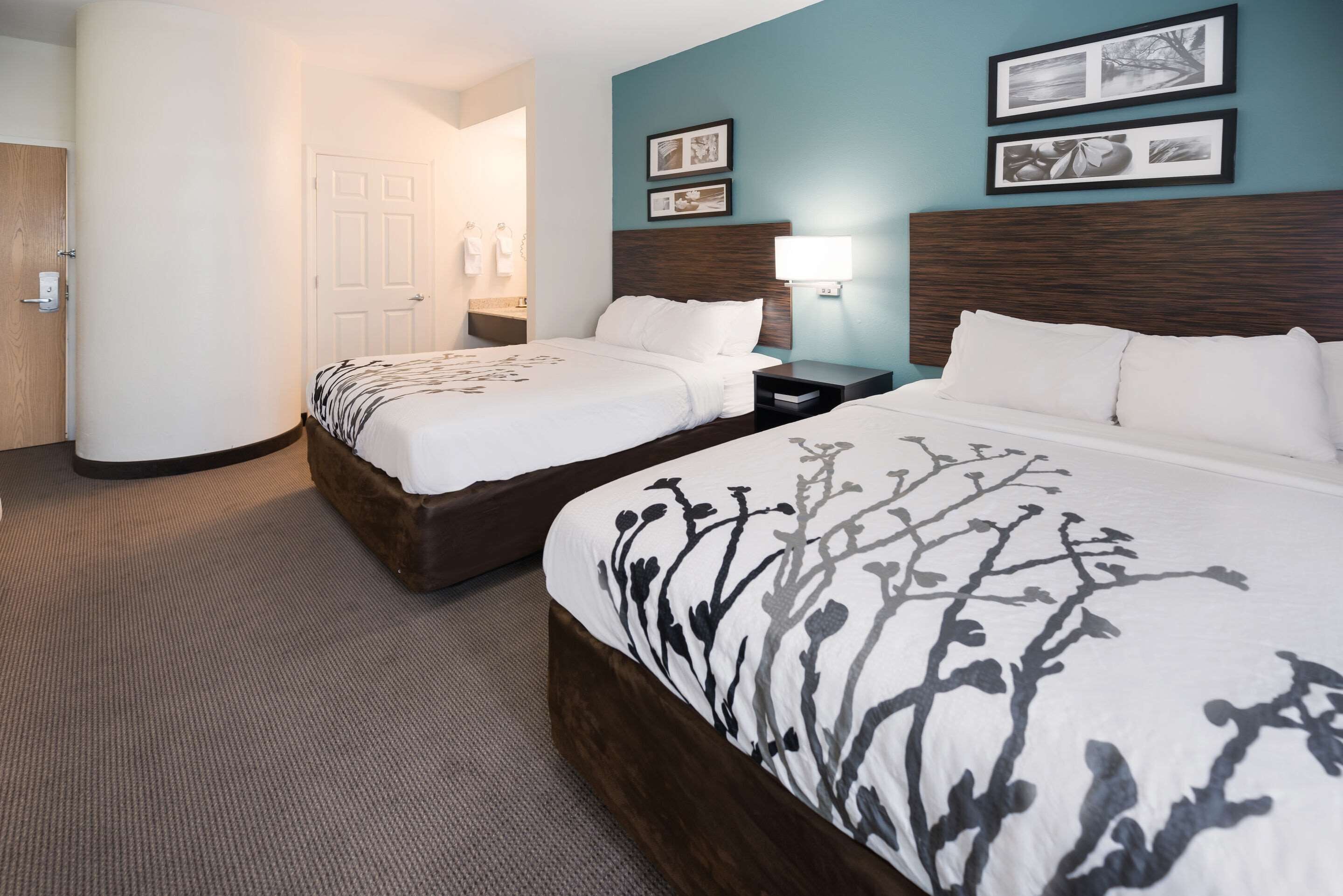 A hotel room with two beds, a nightstand, a lamp, and framed pictures on the wall.