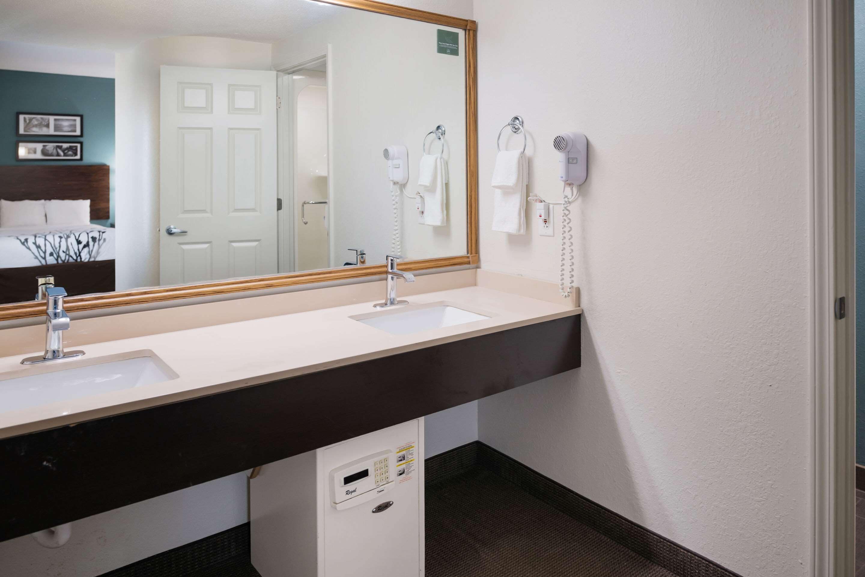 A hotel bathroom with two sinks, a large mirror, a hairdryer, and a towel rack.