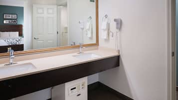 Un baño de hotel con dos lavamanos, un espejo grande, un secador de pelo y un perchero para toallas.