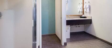 A hotel bathroom with a sink, mirror, towel rack, and a door leading to another room.