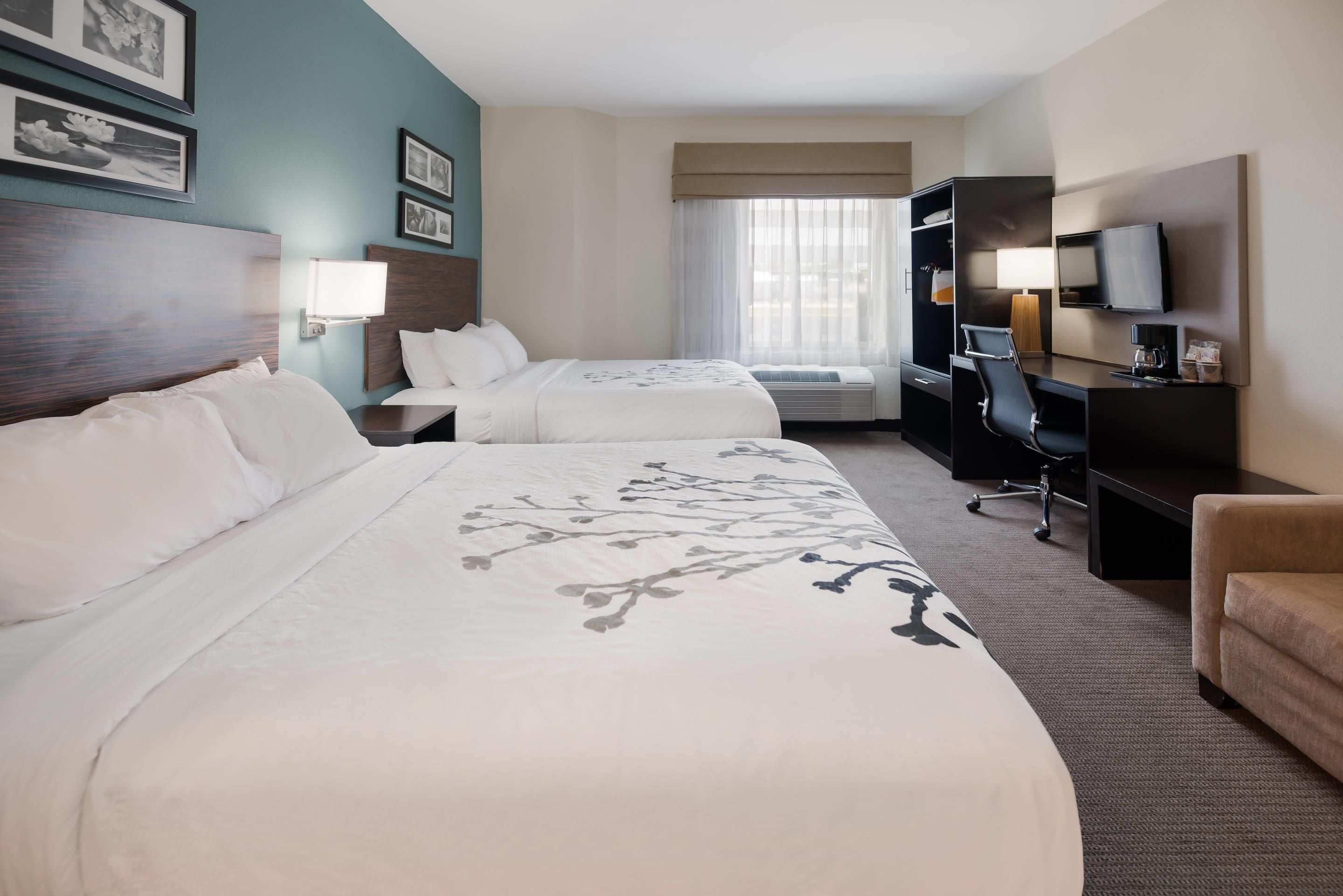 Quarto de hotel com duas camas, uma escrivaninha, uma cadeira, uma televisão e uma janela com cortinas.