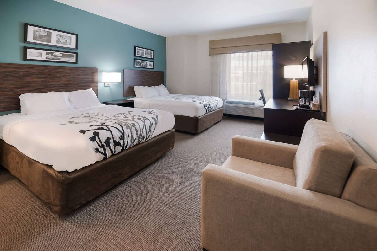 A hotel room with two beds, a sofa, a desk with a lamp, and a TV.