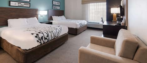 A hotel room with two beds, a sofa, a desk with a lamp, and a TV.