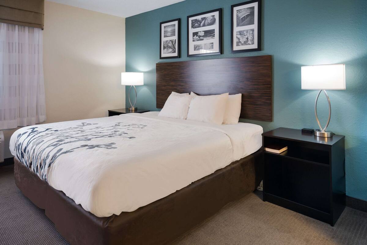 A hotel room with a large bed, two bedside tables, a nightstand, and a wall with framed pictures.