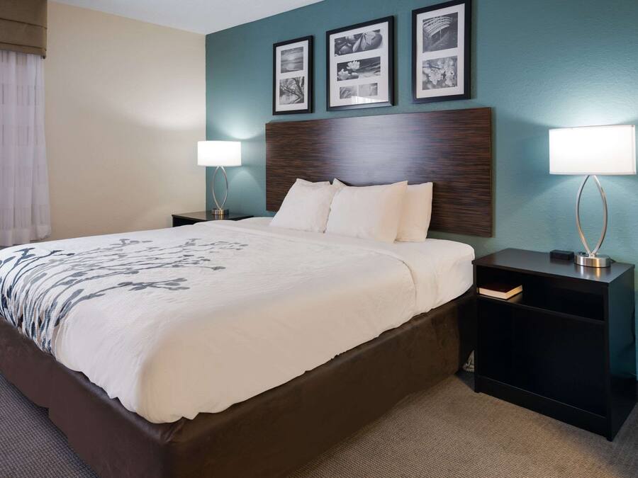 A hotel room with a large bed, two bedside tables, a nightstand, and a wall with framed pictures.