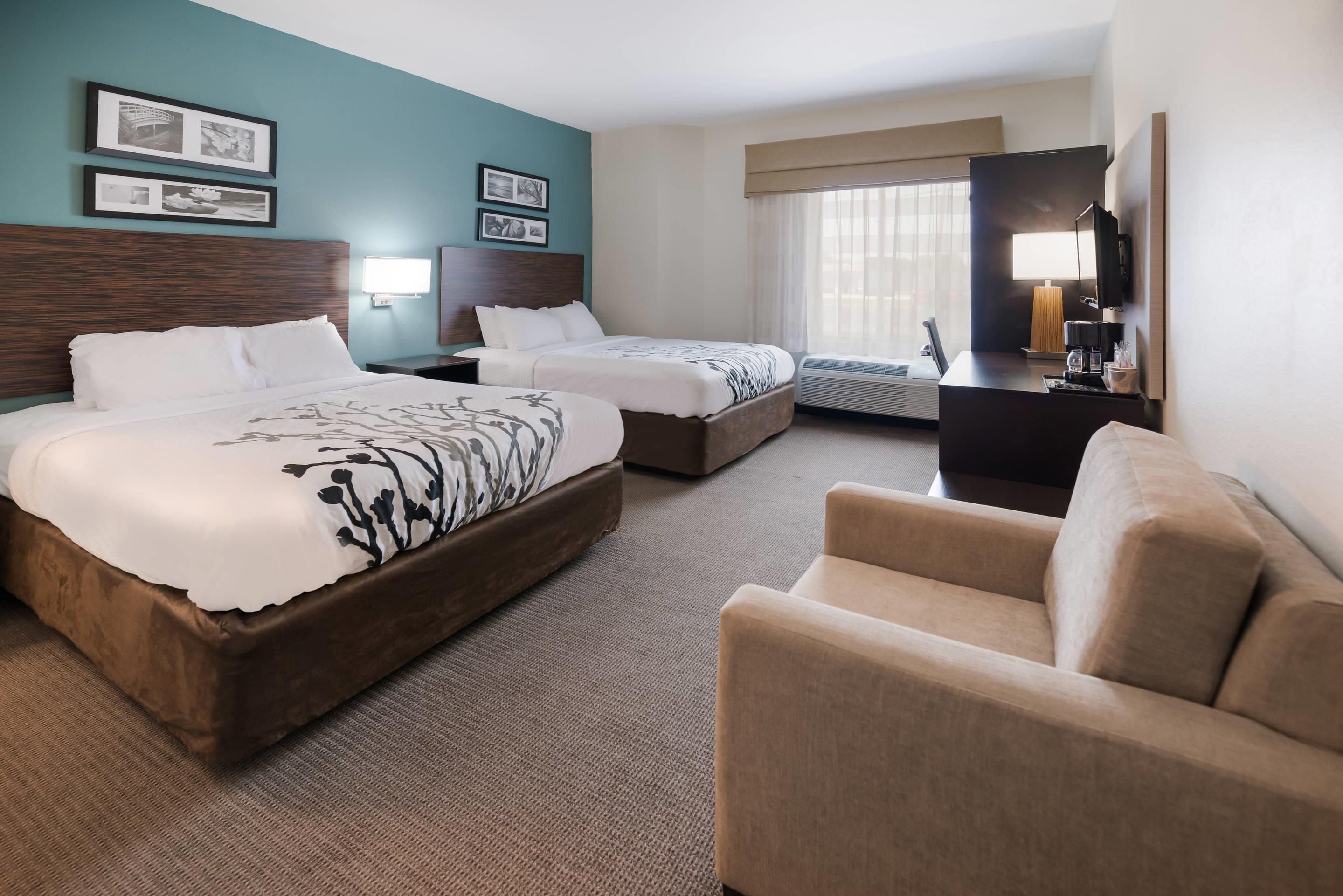 A hotel room with two beds, a sofa, a desk with a lamp, and a TV.
