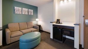 A compact hotel room with a sofa, ottoman, kitchenette, and wall-mounted artwork. - Sleep Inn & Suites Port Clinton (Port Clinton)