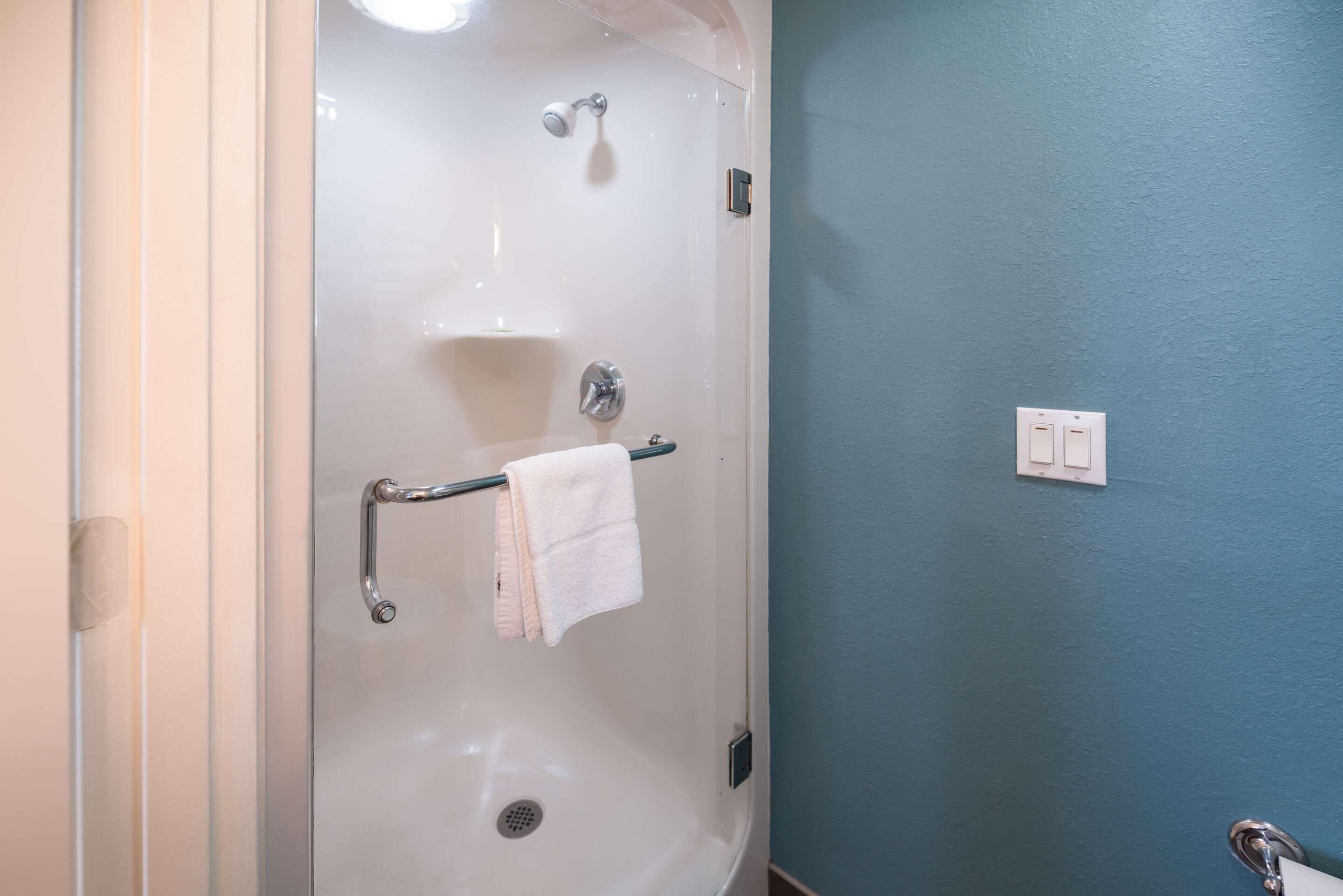 Un baño con ducha envuelta en vidrio, un perchero con una toalla blanca y un interruptor de luz en la pared.