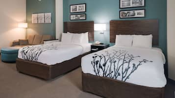 A hotel room with two beds, a sofa, a lamp, and framed pictures on the wall.