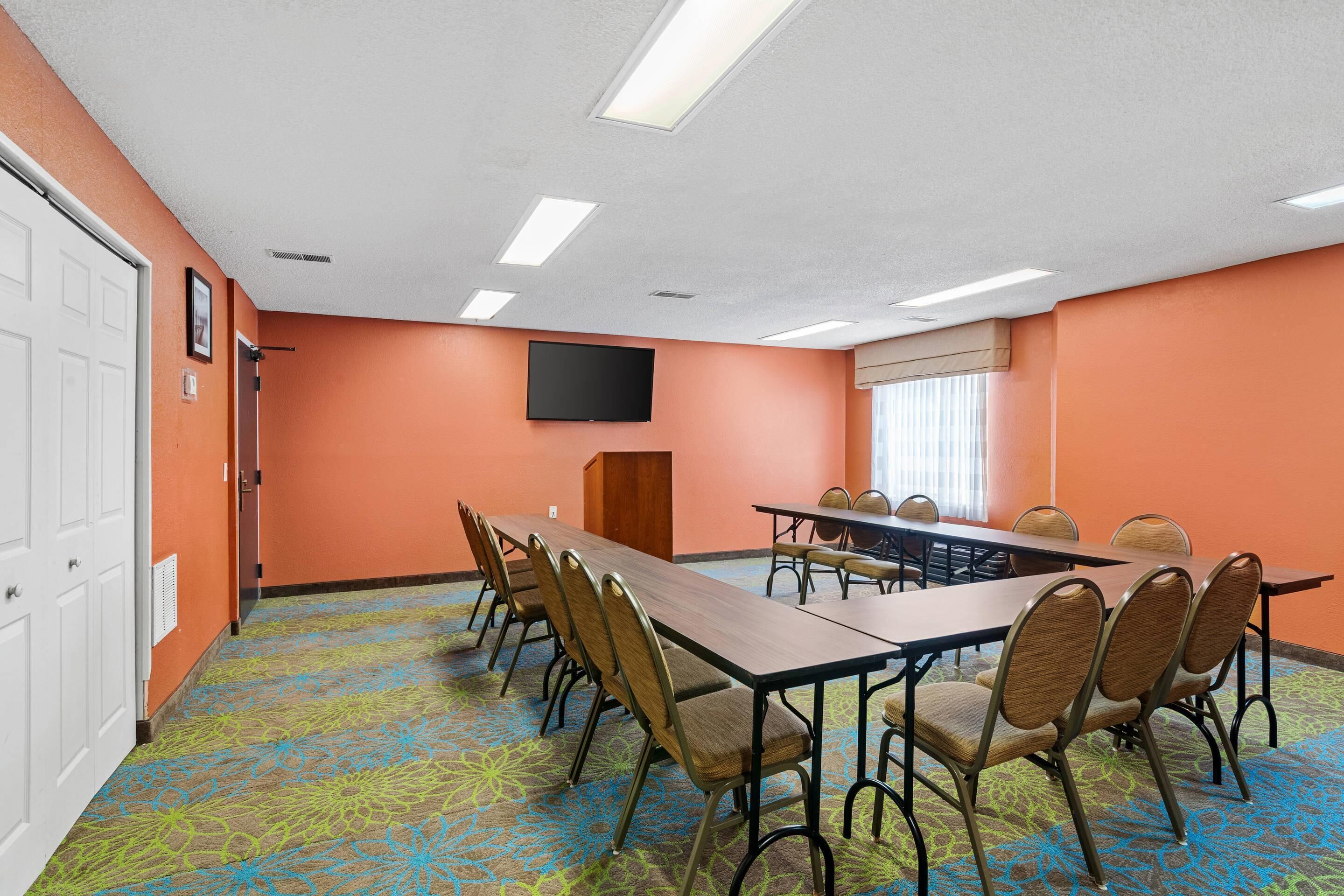 Une salle de conférence avec une longue table, des chaises, un téléviseur à écran plat et une moquette à motifs.