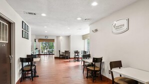 A hotel lobby with wooden flooring, multiple tables and chairs, a clock, and a sign on the wall.