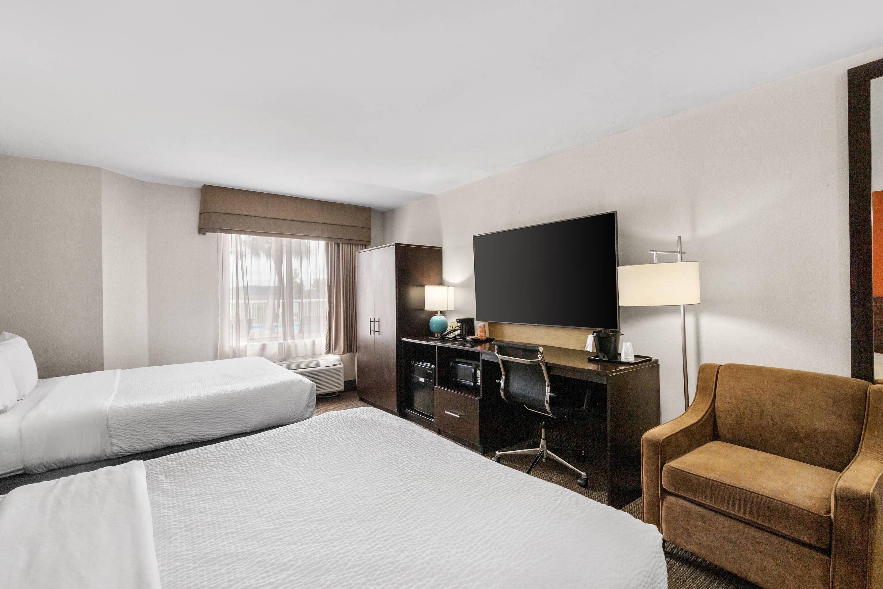 A hotel room with two beds, a desk with a computer, a TV, and a chair.