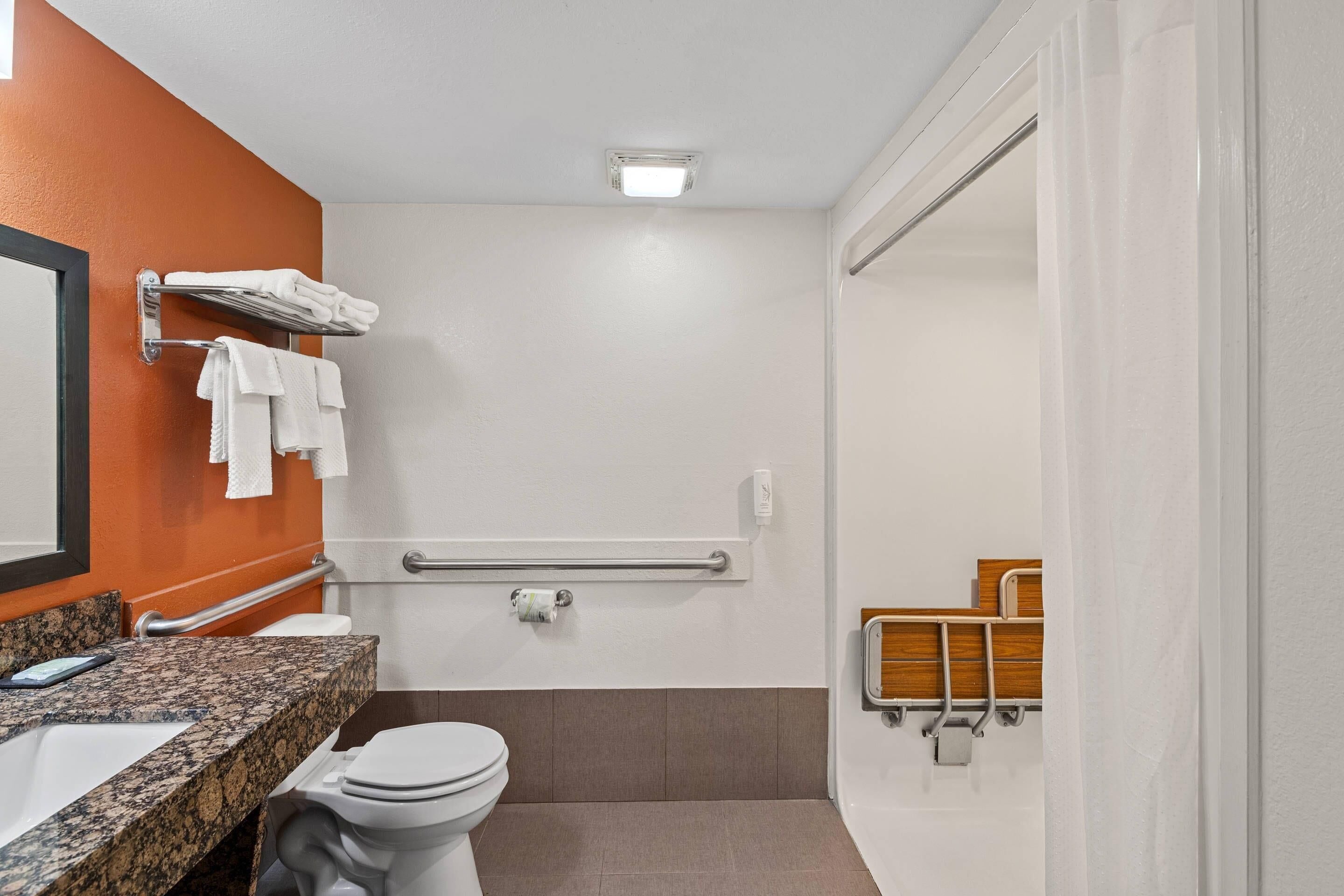 Et badeværelse med toilet, vask, håndklædestang og en bruseafdeling med gelænder.