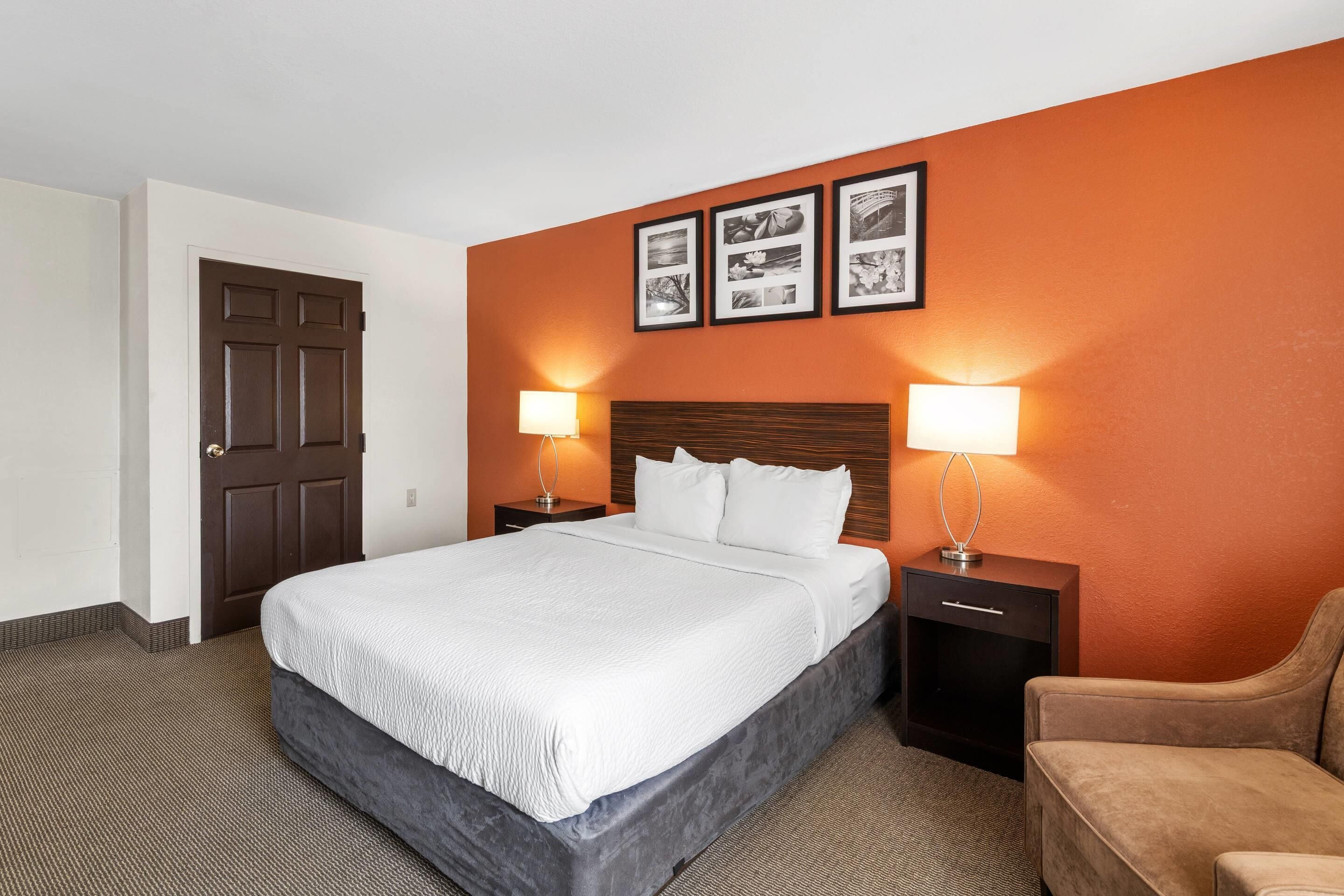 A hotel room with a bed, two bedside tables, a chair, and a door.