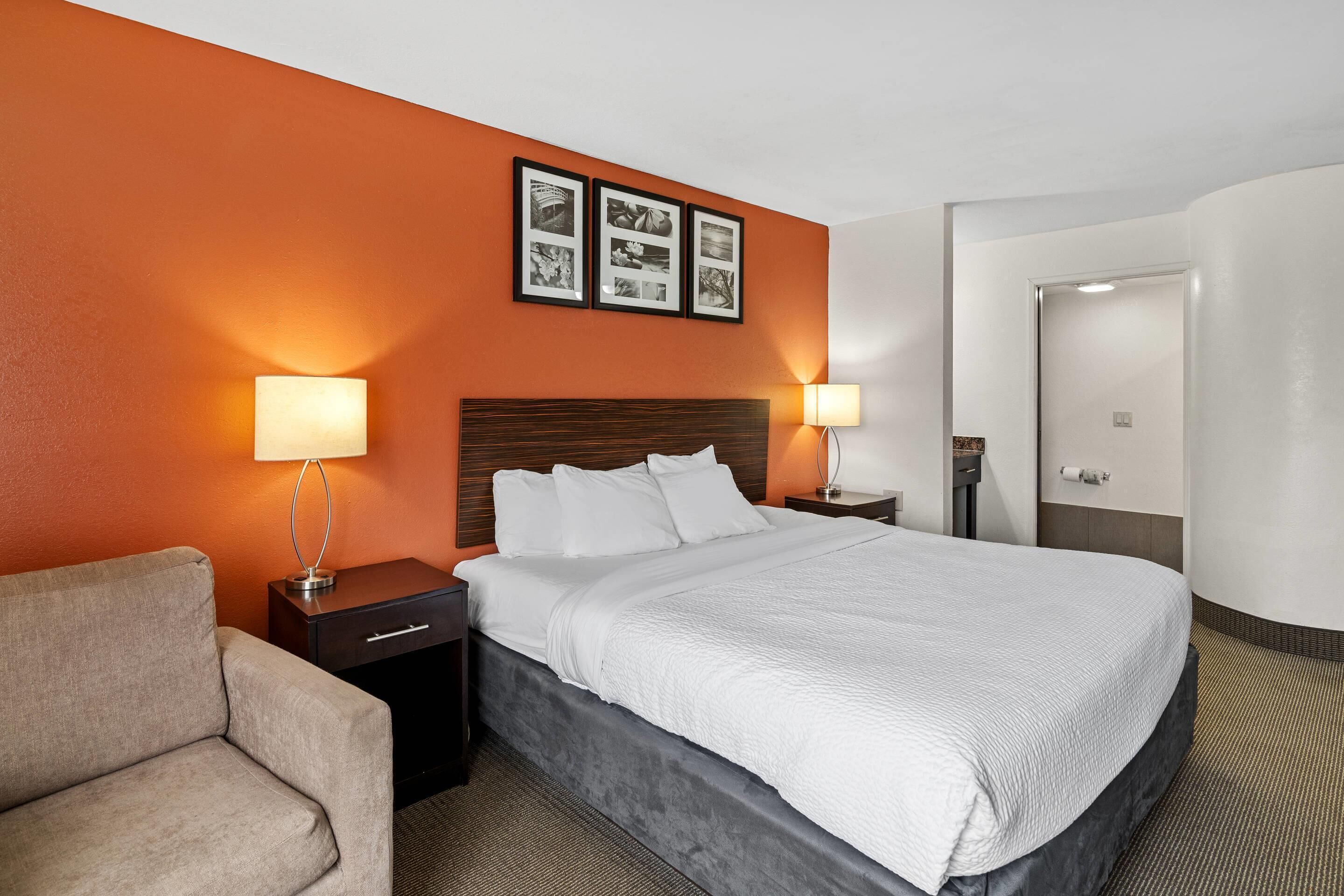 A hotel room with a bed, nightstands, a lamp, a sofa, and framed pictures on the wall.