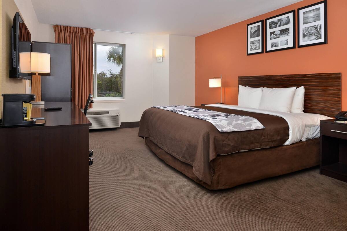 A hotel room with a bed, a desk, a TV, a window with curtains, and framed pictures on the wall.