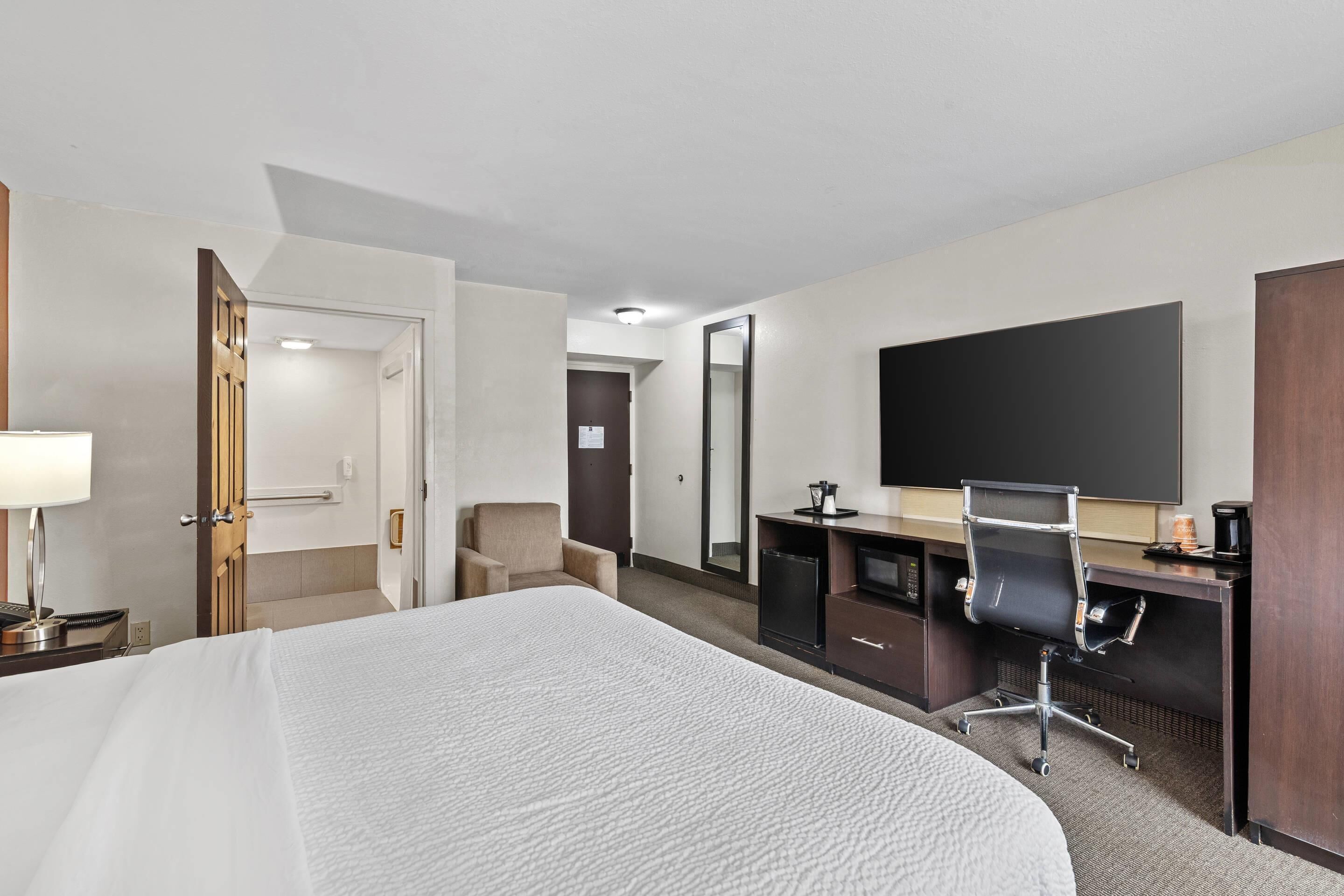 A hotel room with a large bed, a desk with a chair, a flat-screen TV, and a mirror.
