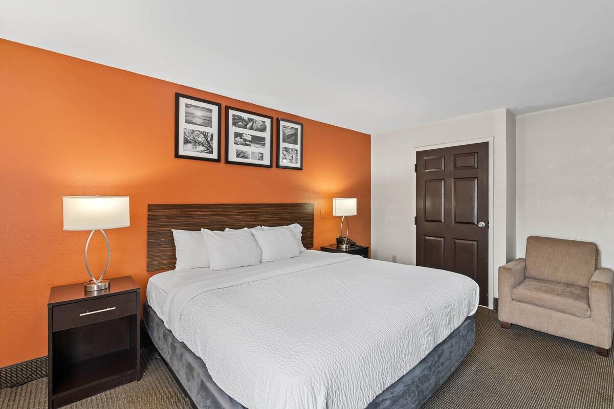 A hotel room with a large bed, two bedside tables with lamps, a chair, and a door.