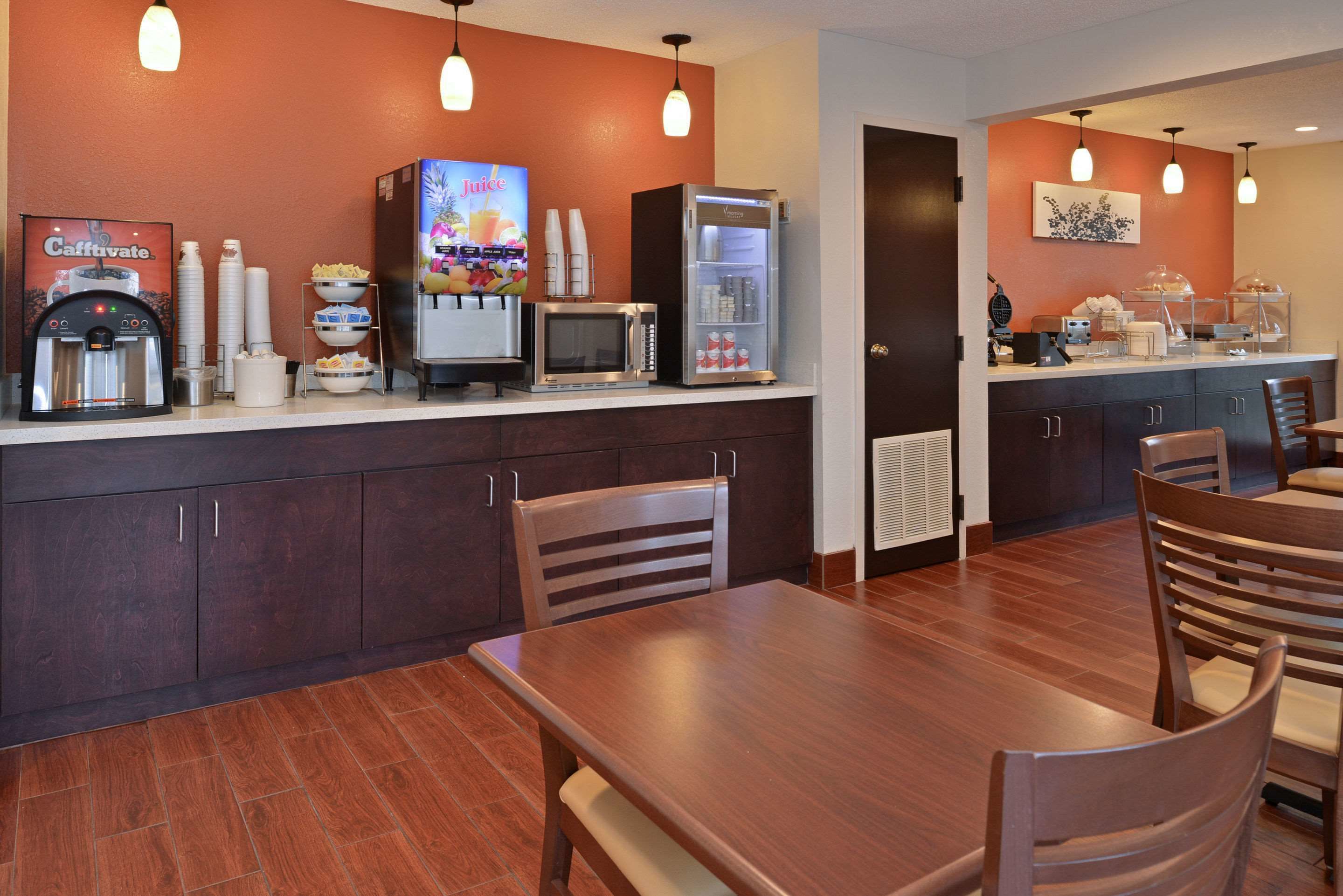 A breakfast bar with a coffee machine, microwave, and refrigerator. There are chairs and a table in the foreground.