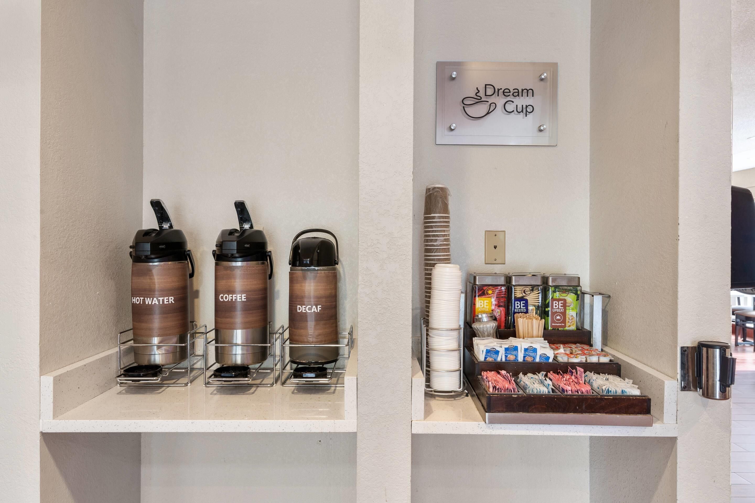 A coffee station with hot water, coffee, and decaf options, and a breakfast bar with various food items and condiments.