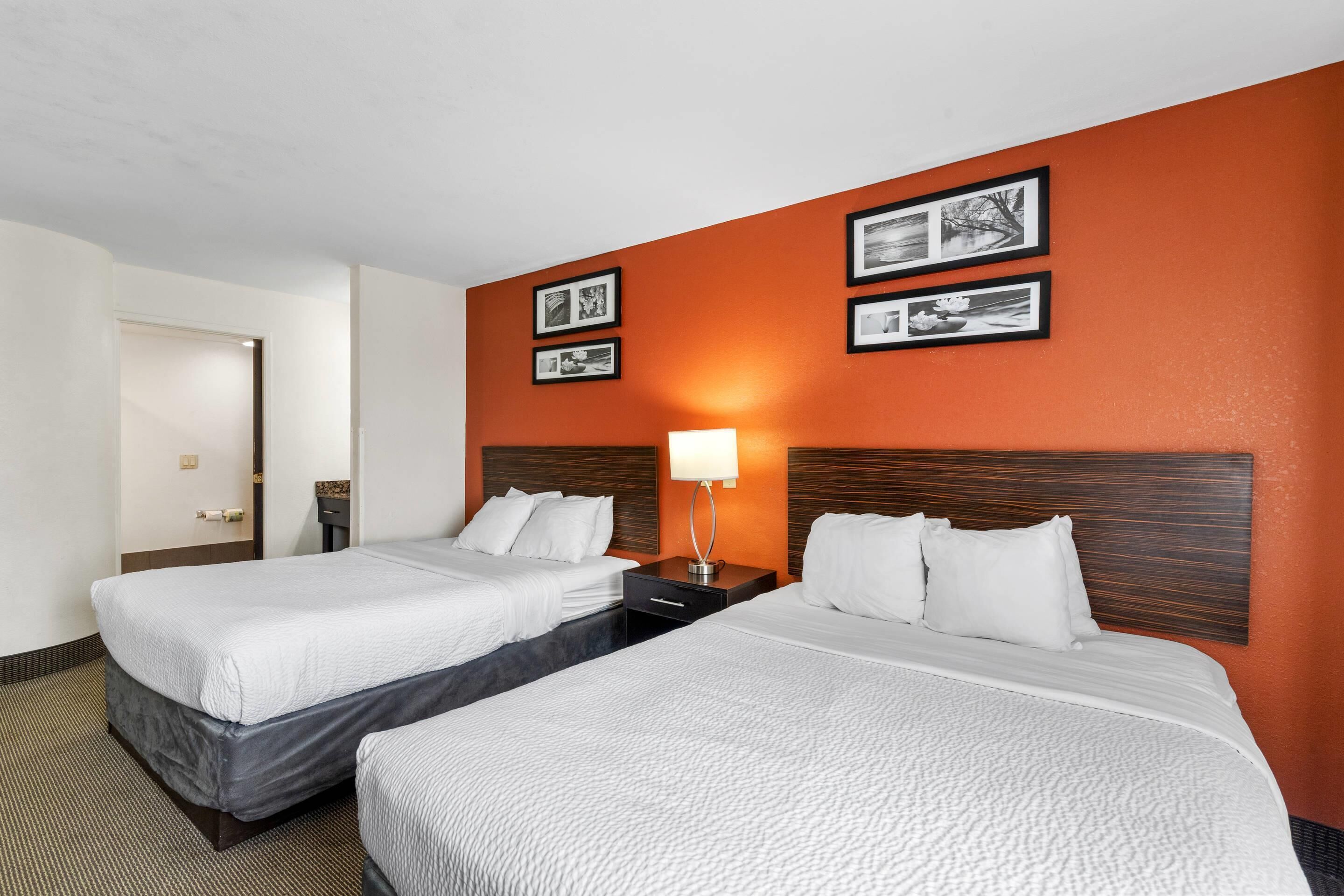 A hotel room with two beds, a nightstand with a lamp, and framed pictures on the wall.