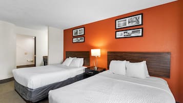 A hotel room with two beds, a nightstand with a lamp, and framed pictures on the wall.