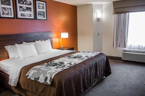 Een hotelkamer met een groot bed, een nachtkastje met een lamp, een wandairconditioner en ingelijste foto's aan de muur.