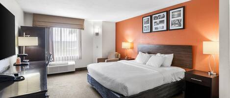 A hotel room with a bed, bedside tables, a desk, a TV, and a window with curtains.