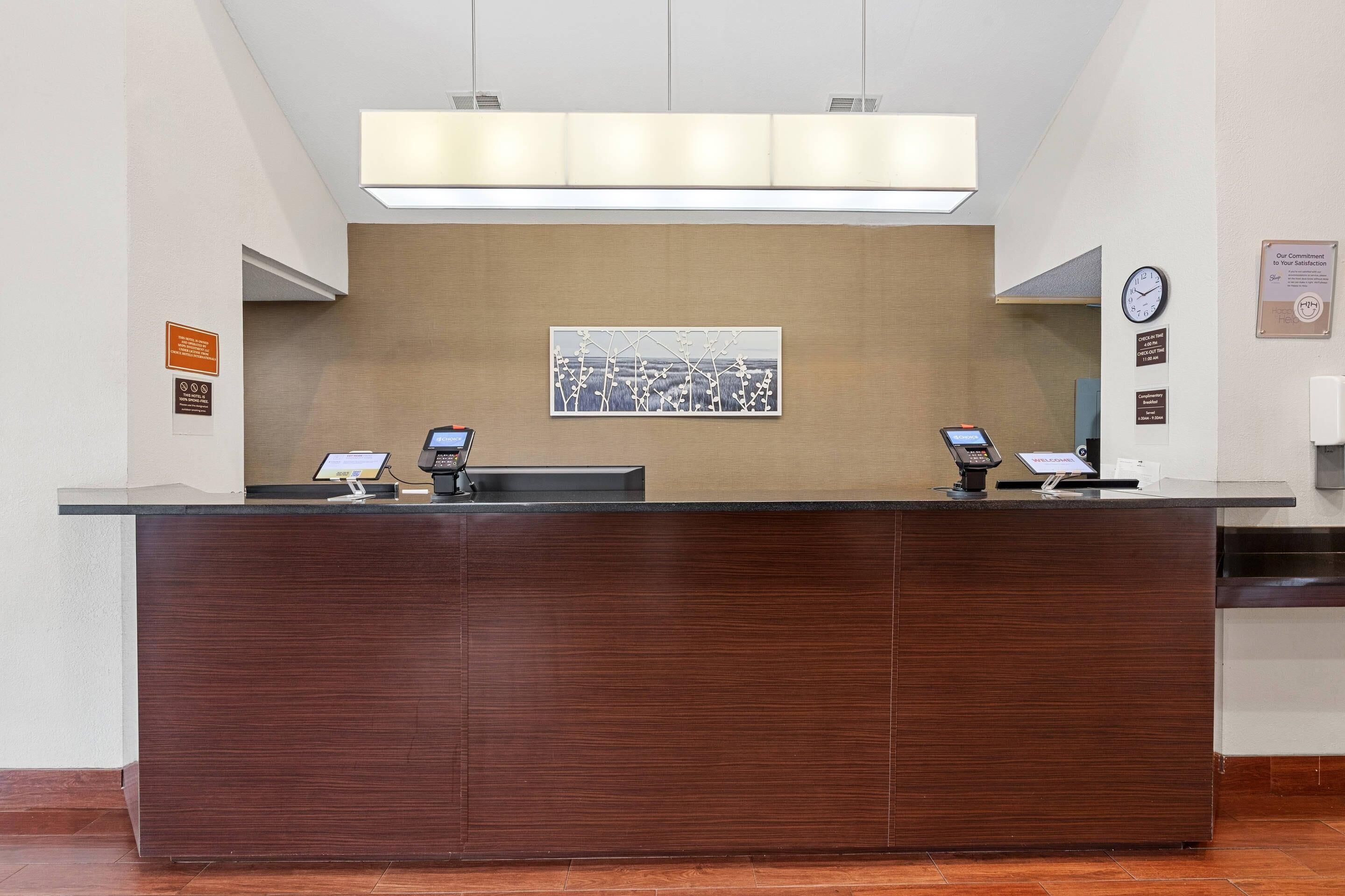 A reception desk with two computer monitors, a clock, and a framed picture on the wall.