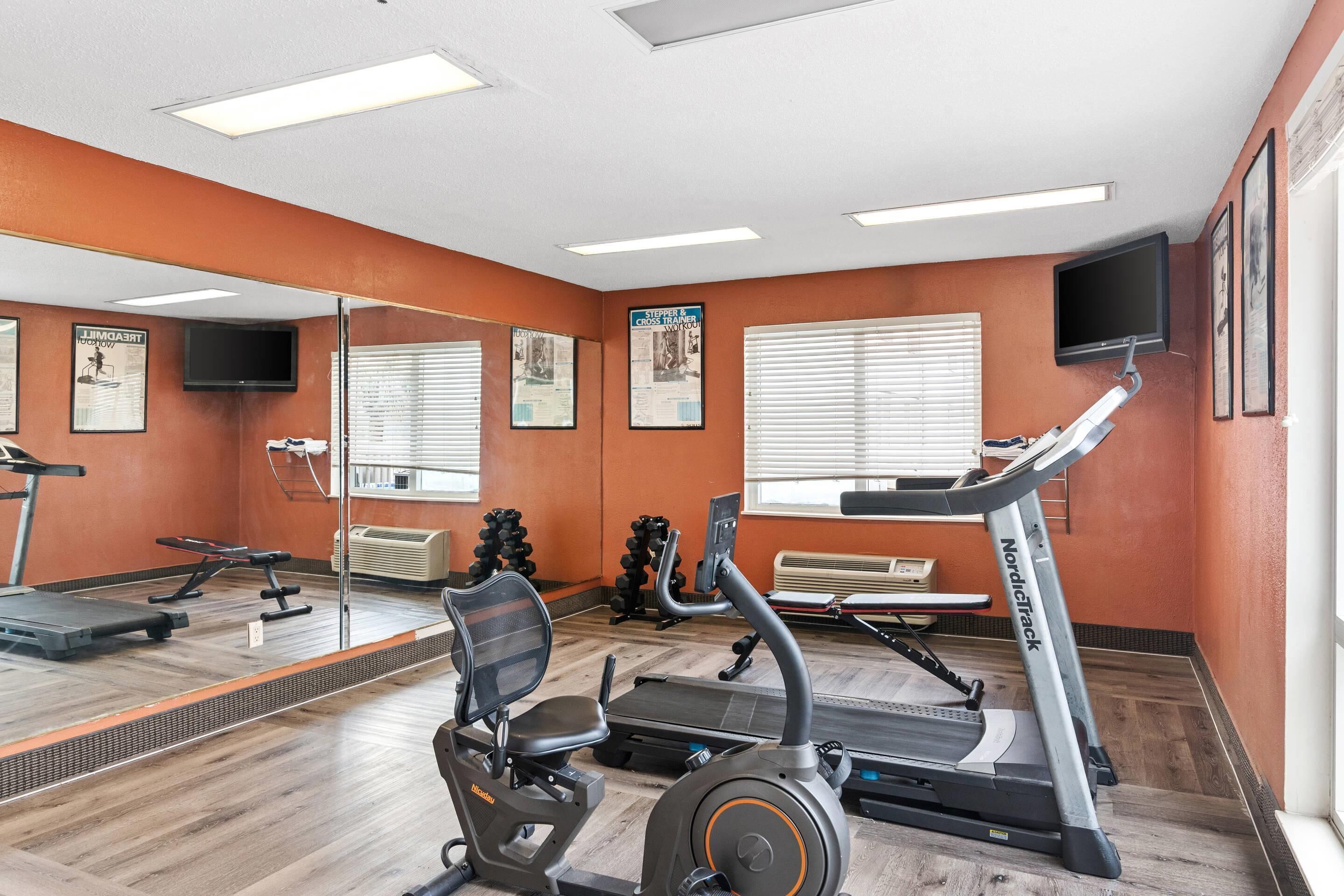 Ein Fitnessraum mit Trainingsgeräten, einem Spiegel und einem Fernseher an der Wand.