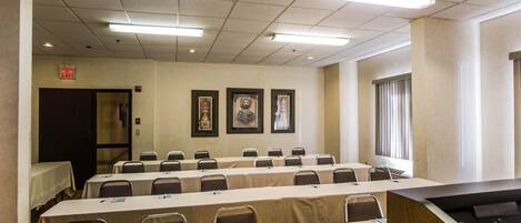 A conference room with long tables, chairs, framed pictures on the wall, and an exit sign.