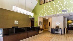 A reception area with a dark wooden reception desk, a green wall with a white branch design, and a sign for 'Sleep Inn'. - Sleep Inn Columbia Airport (West Columbia)