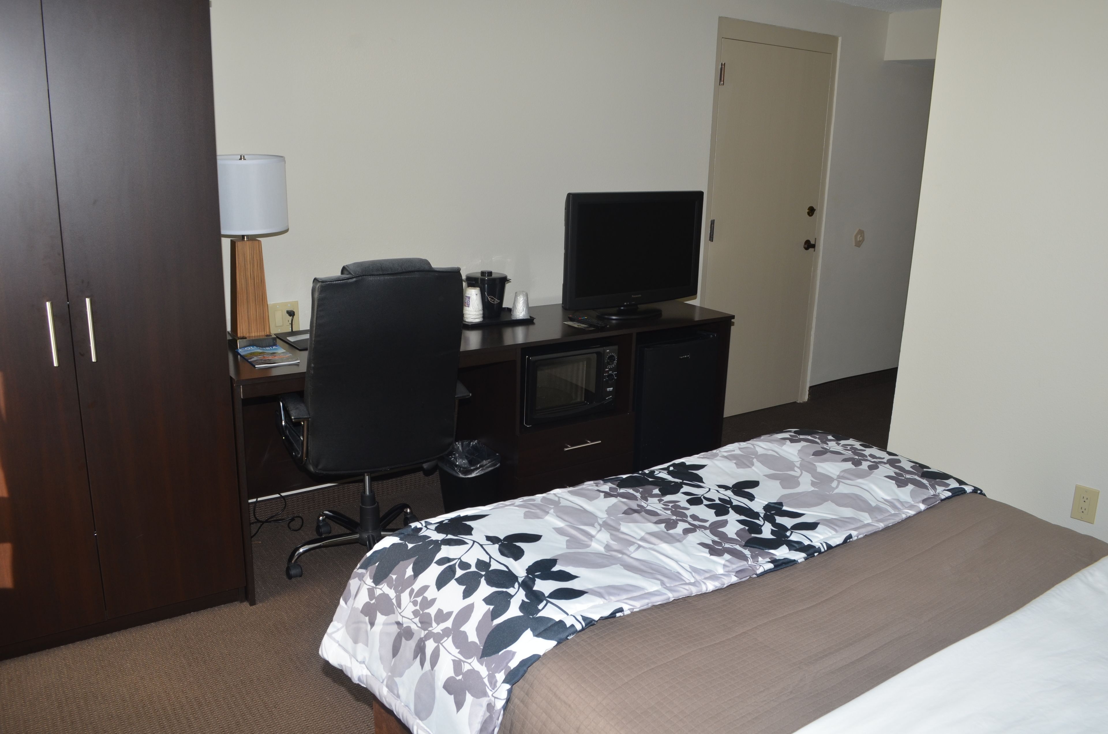 A hotel room with a bed, a desk with a computer, a television, and a lamp.