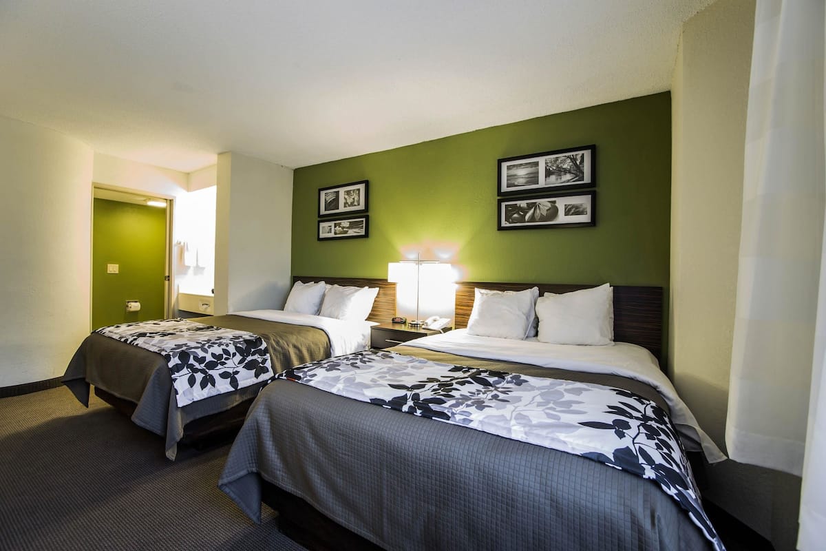 A hotel room with two beds, a green accent wall, framed pictures, and a nightstand with a lamp.