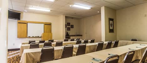 Una sala de conferencias con mesas y sillas largas, una pizarra y un televisor en la pared.