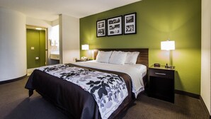 A hotel room with a large bed, two bedside tables with lamps, a green accent wall, and framed pictures above the bed. - Sleep Inn Columbia Airport (West Columbia)