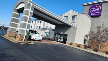A Sleep Inn & Suites by Choice Hotels building with a modern design, including a distinctive arched entrance and a parking area.